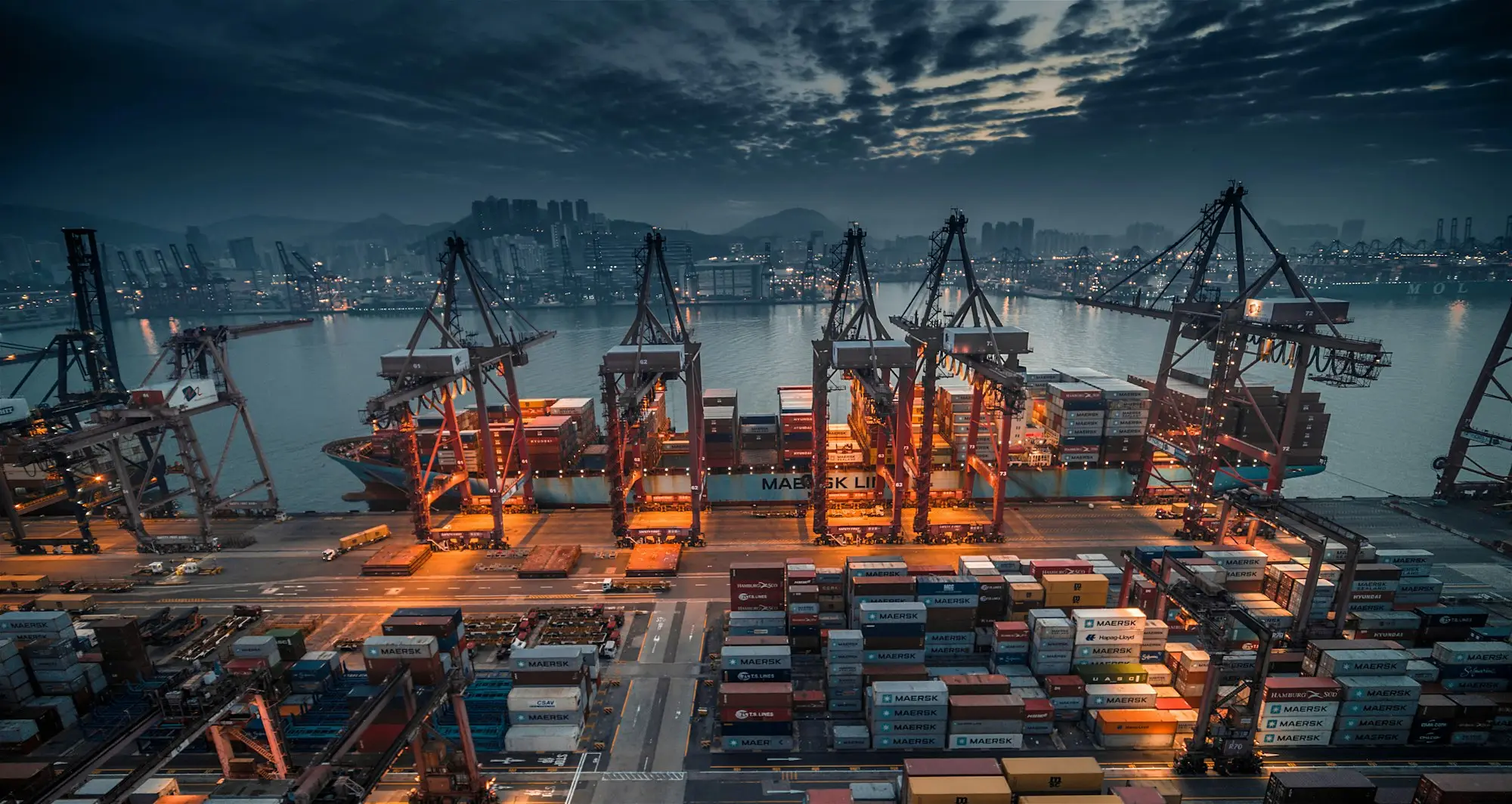 Container ship being loaded by cranes at a busy port at dusk