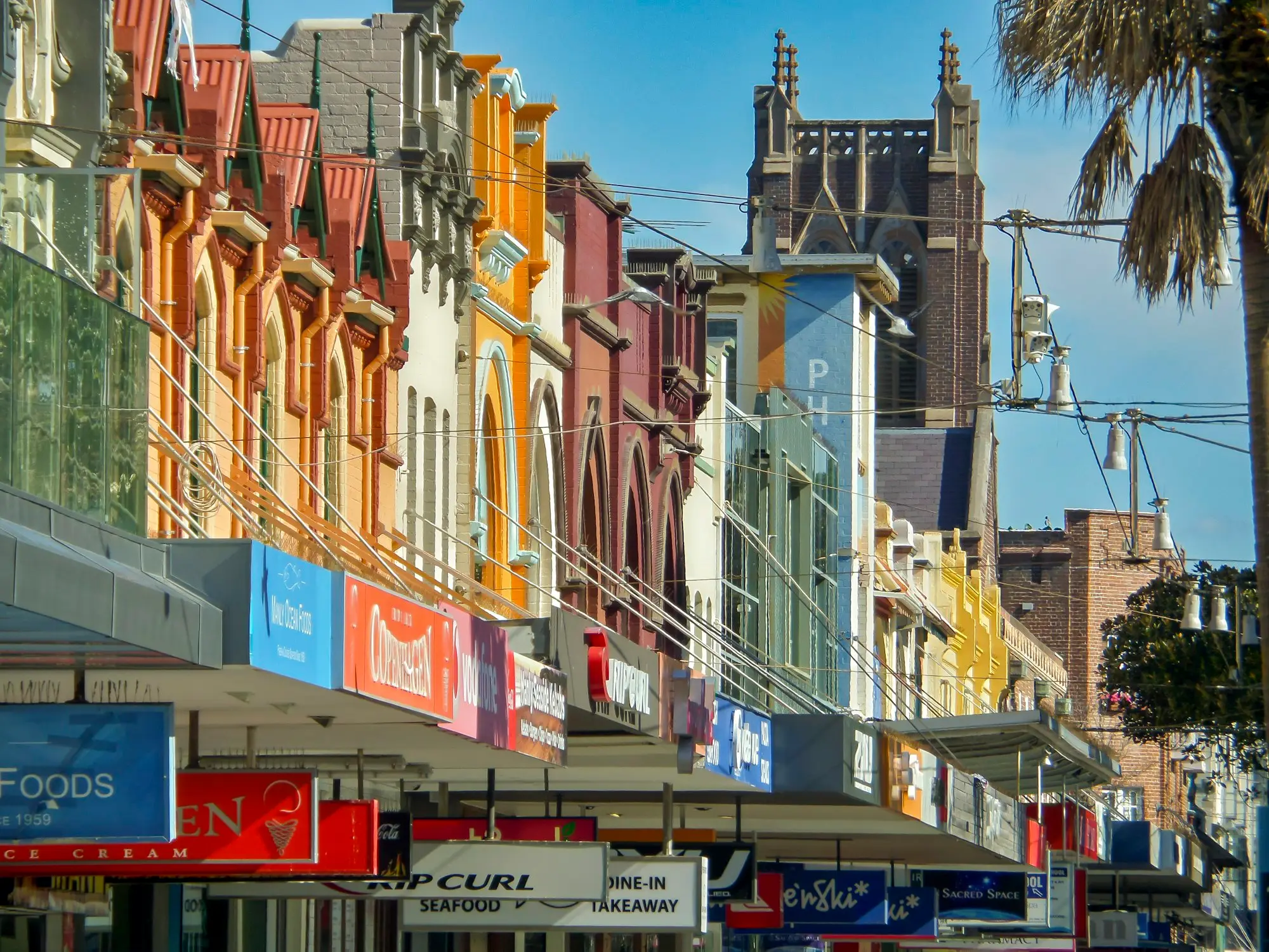 Row of colourful heritage shopfronts on a busy street in Manly, NSW